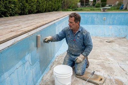Professionnel appliquant une résine d'étanchéité sur les parois en béton d'une piscine vide avant rénovation estivale
