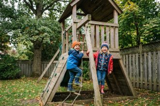 Deux enfants rient en jouant sur une structure en bois dans un jardin