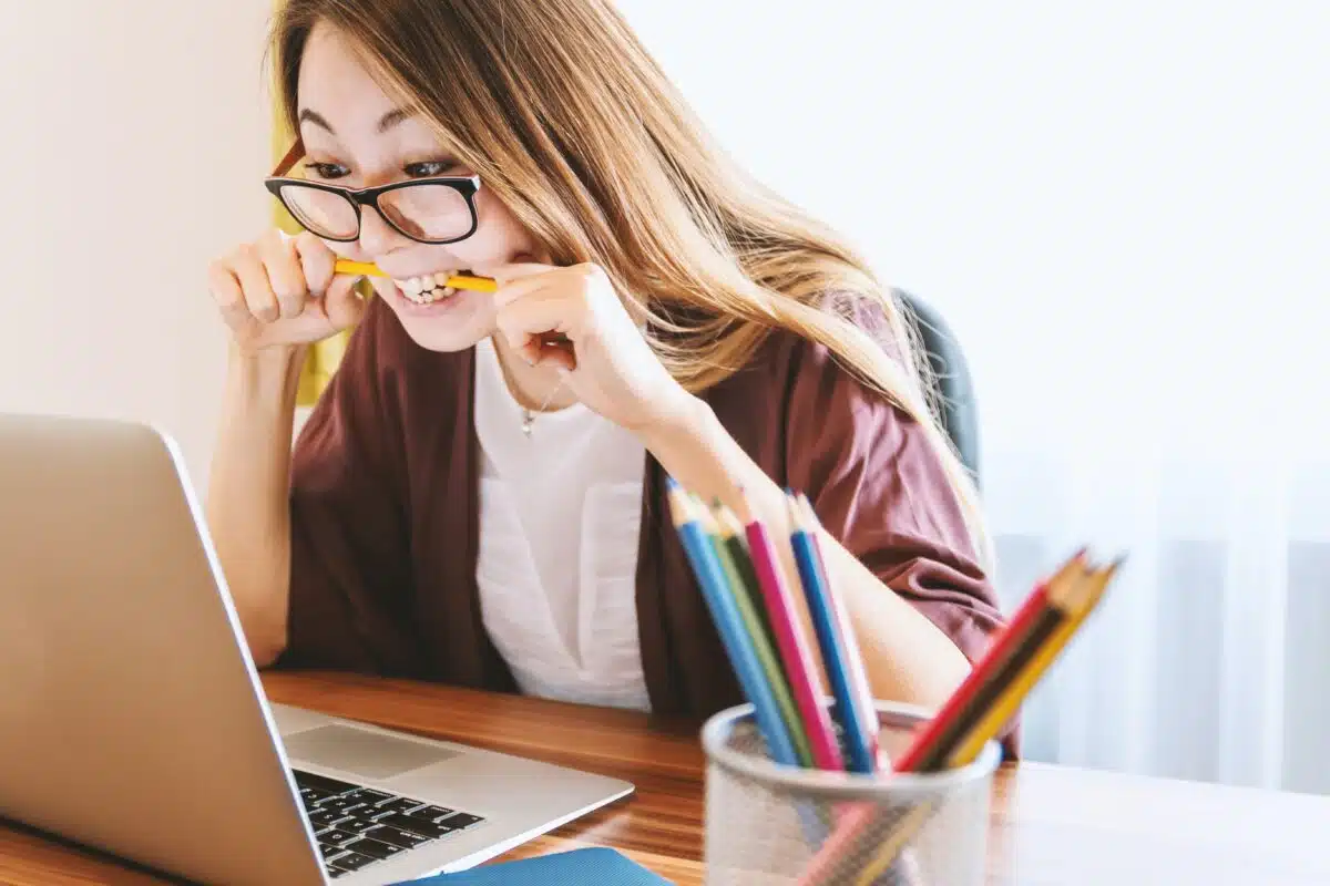 une femme mordant un crayon devant son PC