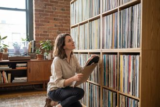 Femme organisant sa collection de vinyles dans un salon vintage avec étagères en bois et platine rétro